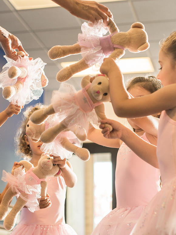 Children playing with teddy bears dressed in ballet outfits.